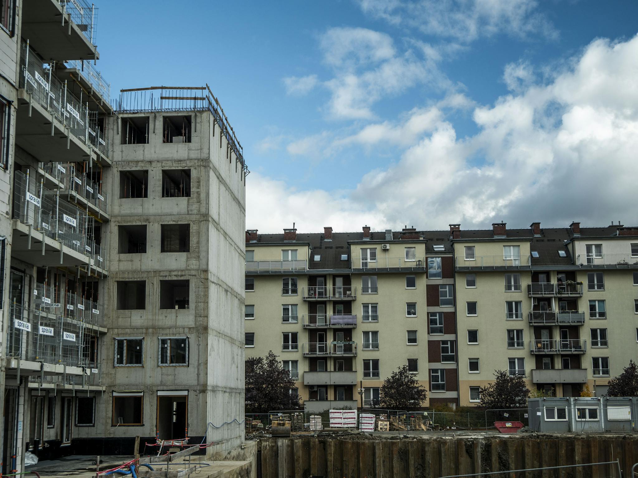 Construction site beside residential buildings under blue skies.