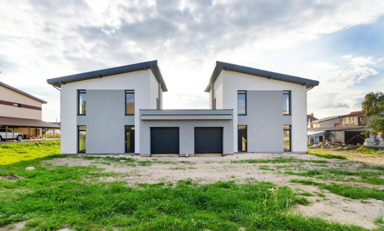 Front view of twin modern houses with a symmetrical architectural design under a cloudy sky.