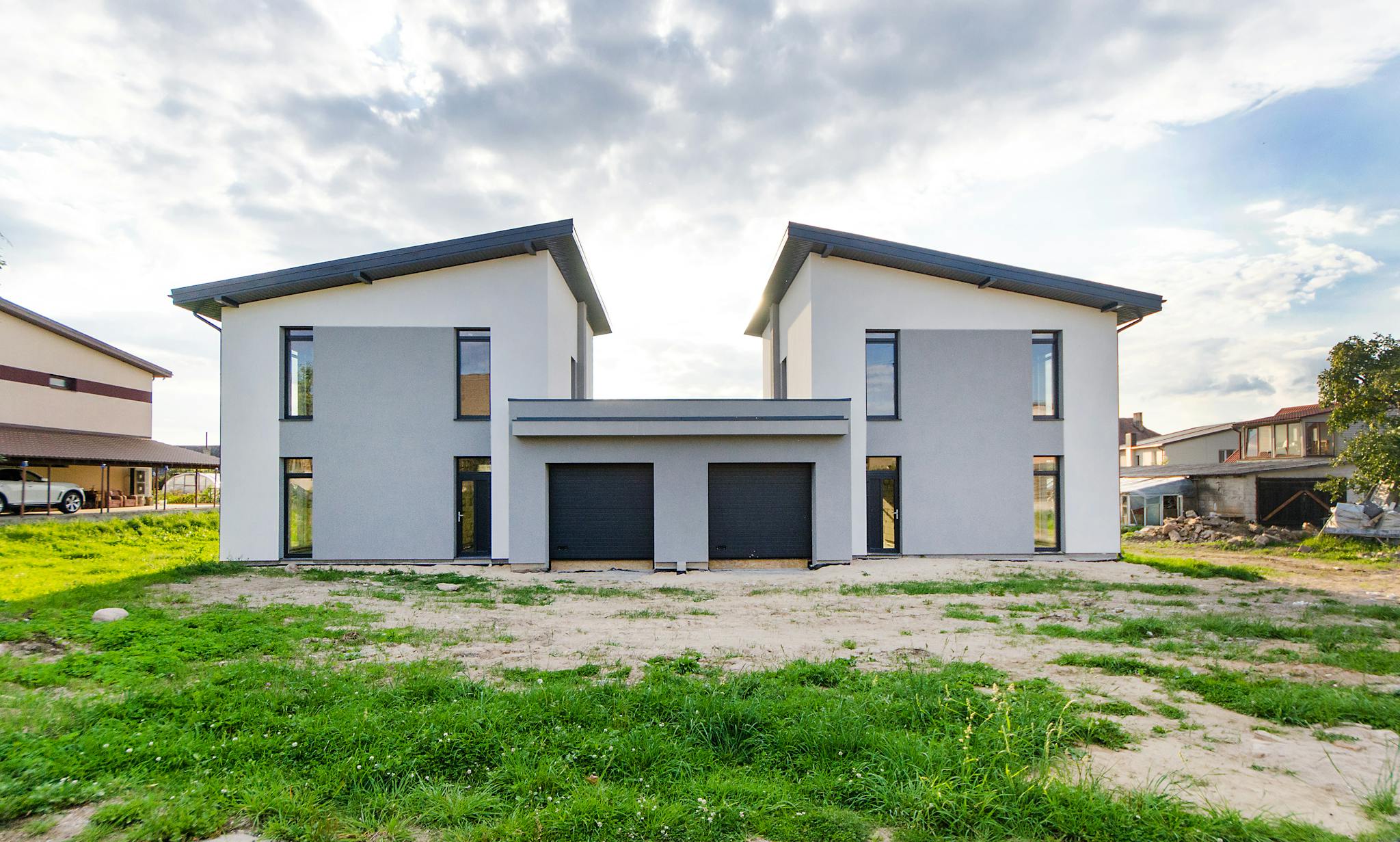Front view of twin modern houses with a symmetrical architectural design under a cloudy sky.